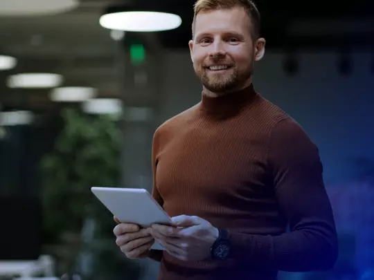 uśmiechnięty mężczyzna z brodą w wiśniowym golfie trzymający tablet