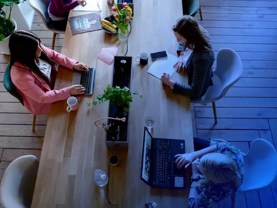 osoby siedzące przy drewnianym biurku przy laptopach