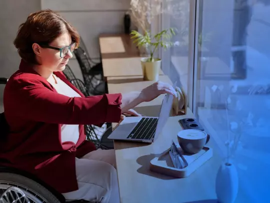 osoba siedząca na wózku inwalidzkim obsługująca komputer