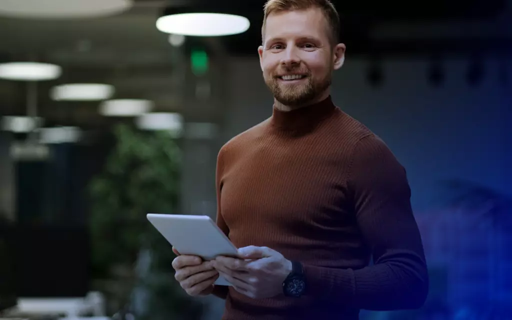 uśmiechnięty mężczyzna z brodą w wiśniowym golfie trzymający tablet