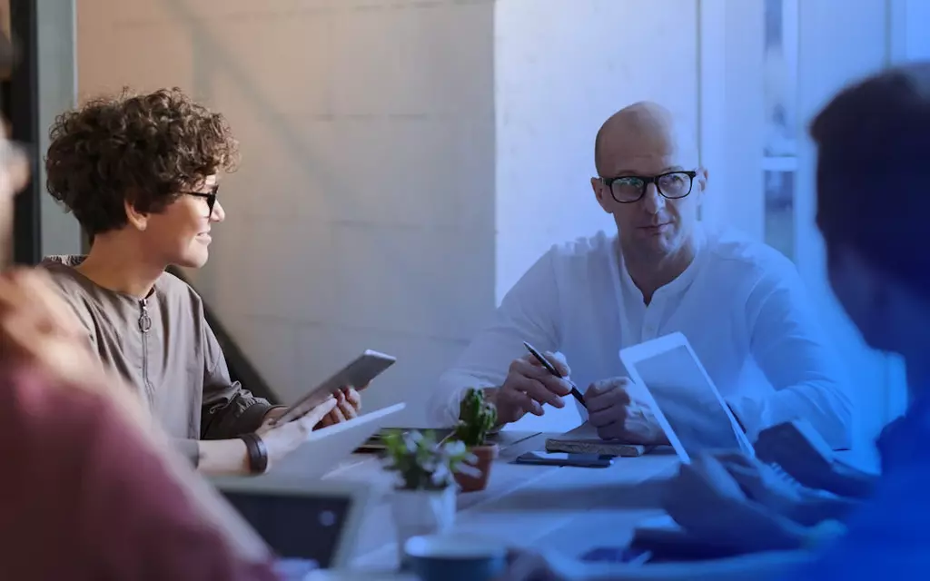 ludzie siedzący przy biurku trzymający tablety w rękach